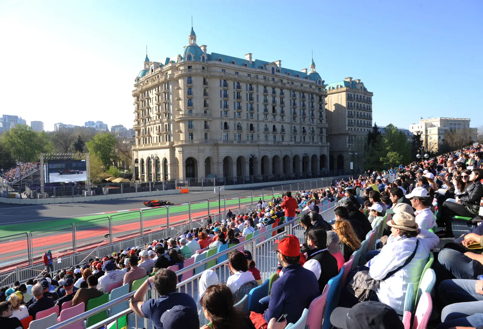 Fans in a Baku grandstand watch an F1 car pass the Four Seasons hotel