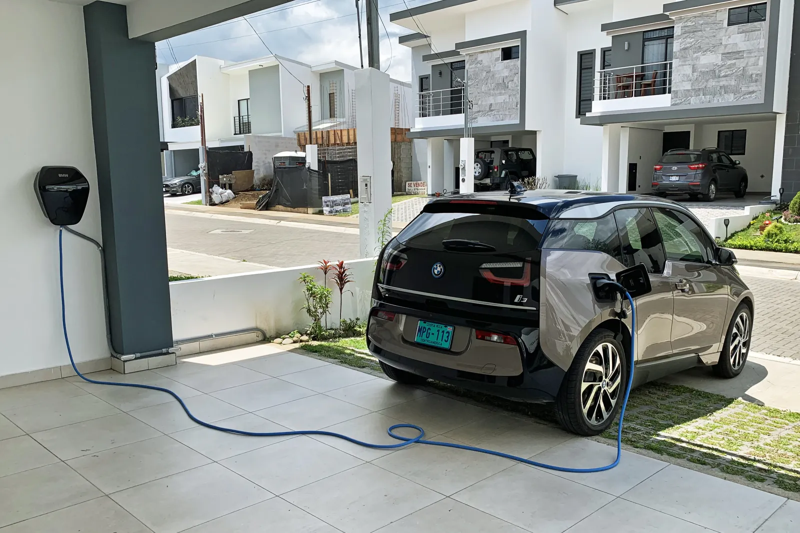 BMW i3 charging from a wall-mounted Level 2 box under a home carport