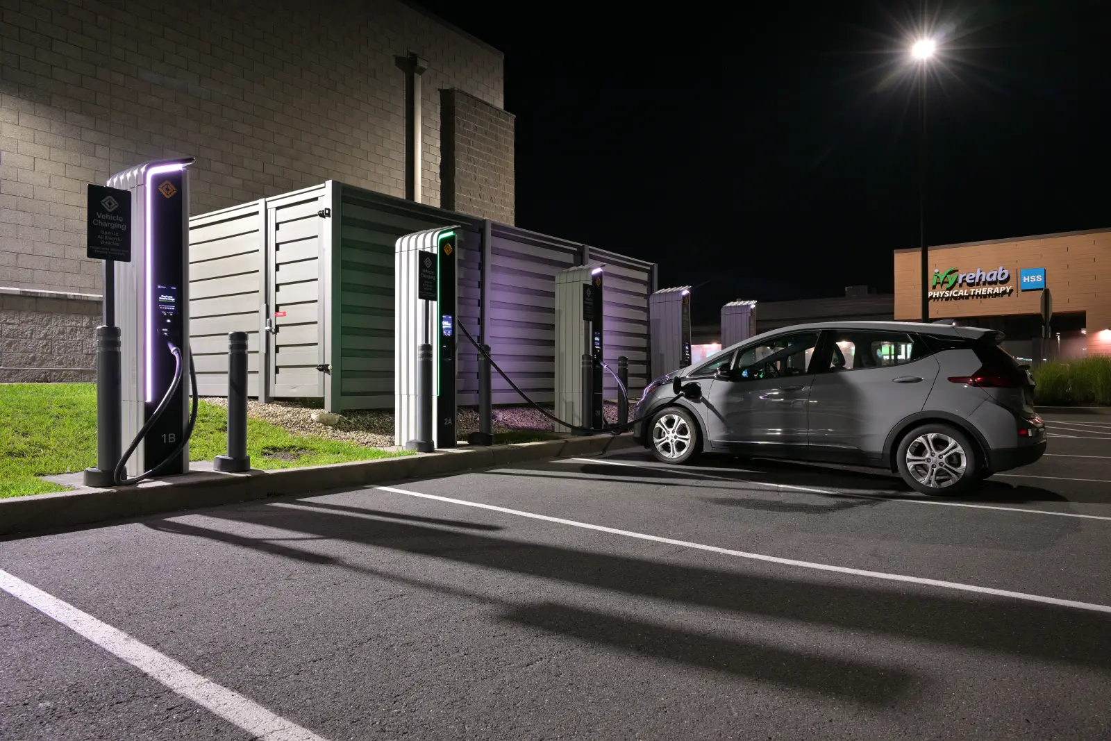 Silver Chevrolet Bolt EV plugged into a DC fast charger at night in a car park
