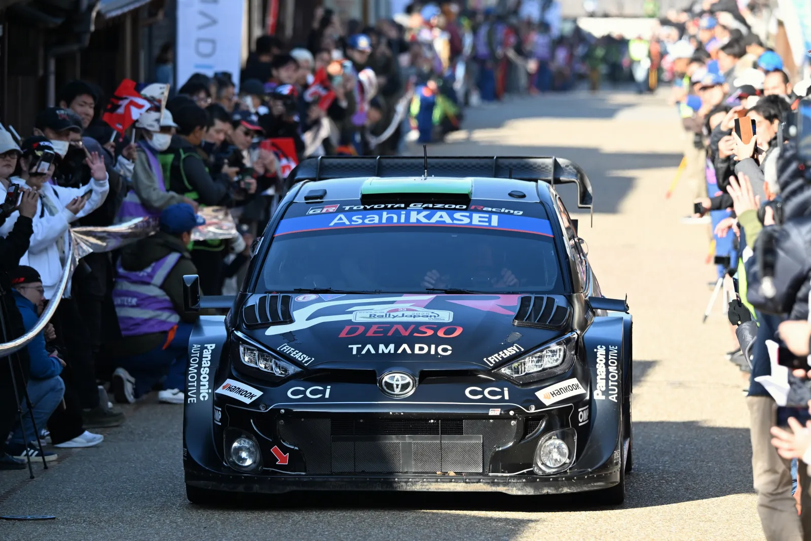 Elfyn Evans's number 33 Toyota GR Yaris Rally1 on a street liaison surrounded by fans