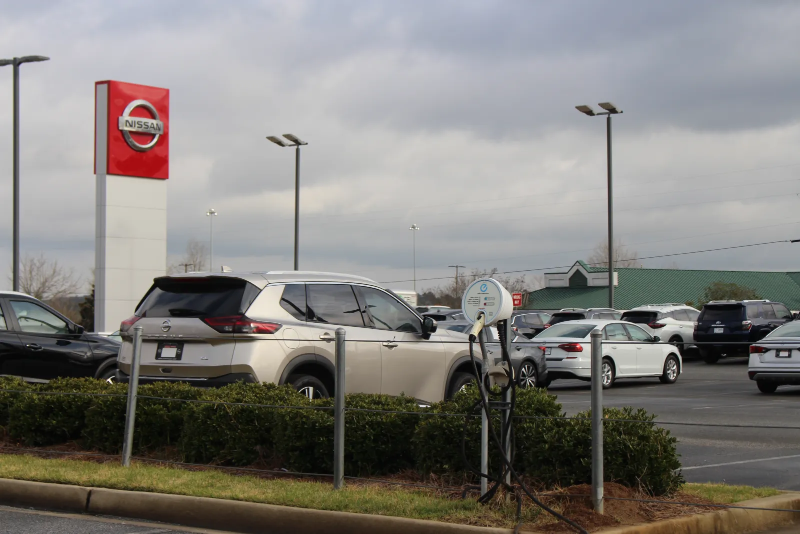 Electric vehicle charging post beside new cars on a Nissan dealership lot in Georgia