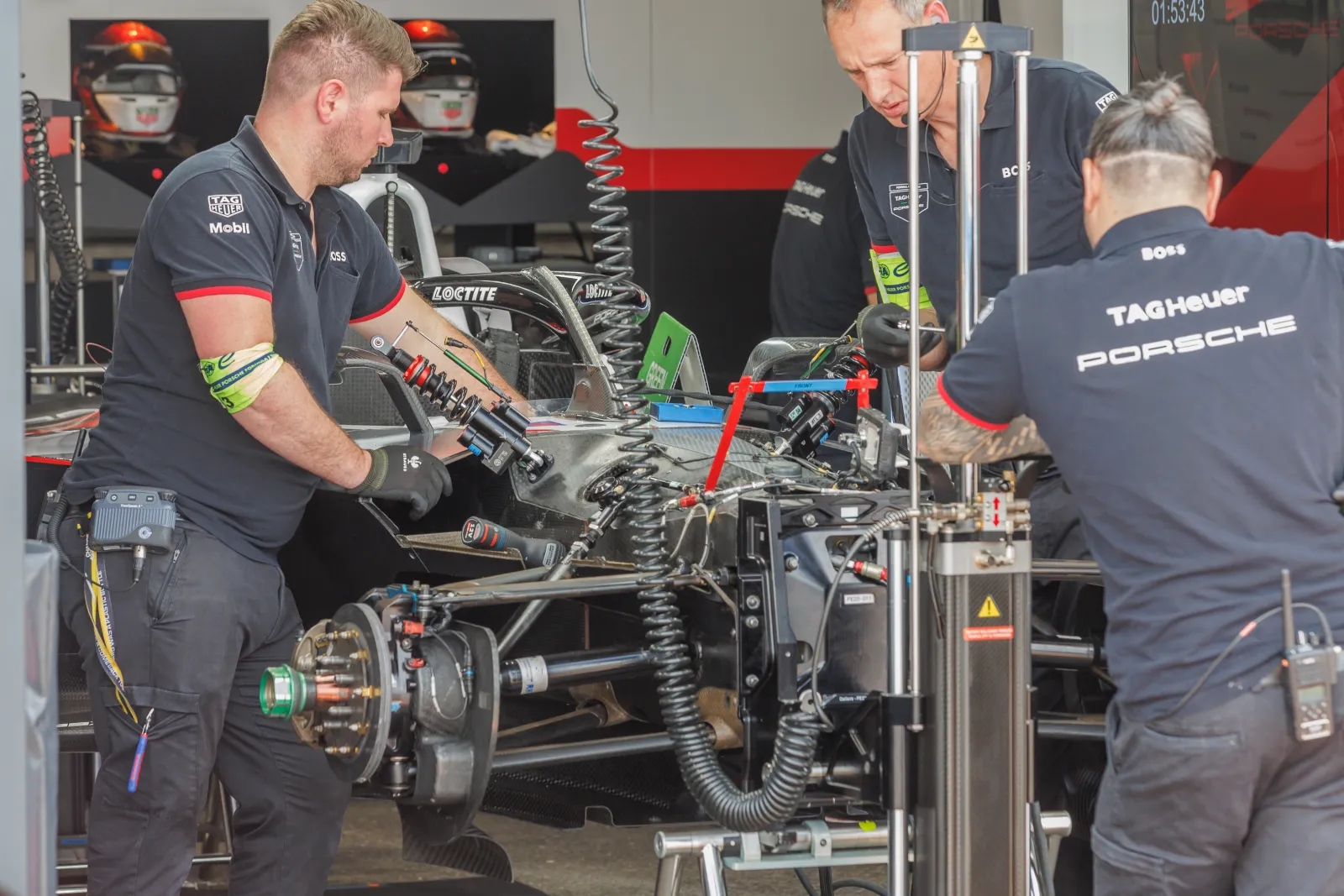 Porsche mechanics working on the exposed front suspension of a Formula E car in the garage