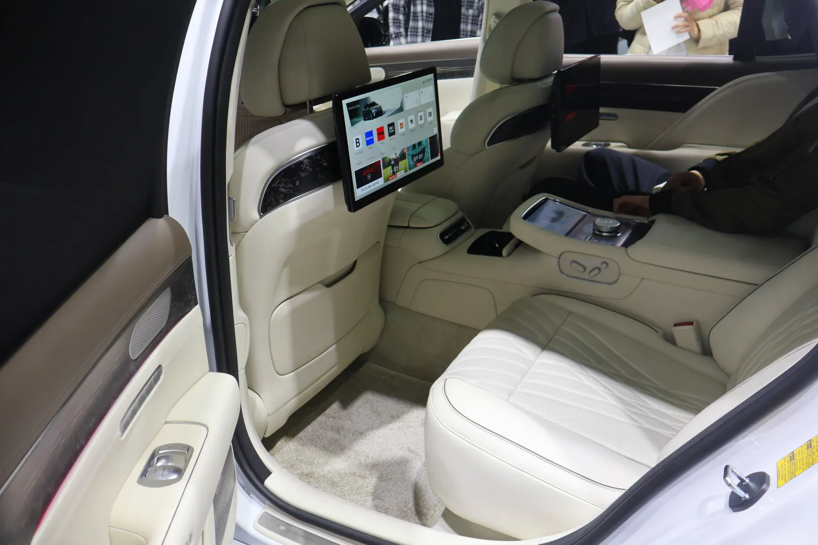 Bancos traseiros de um sedã Genesis G90 em couro creme, com tela para o passageiro