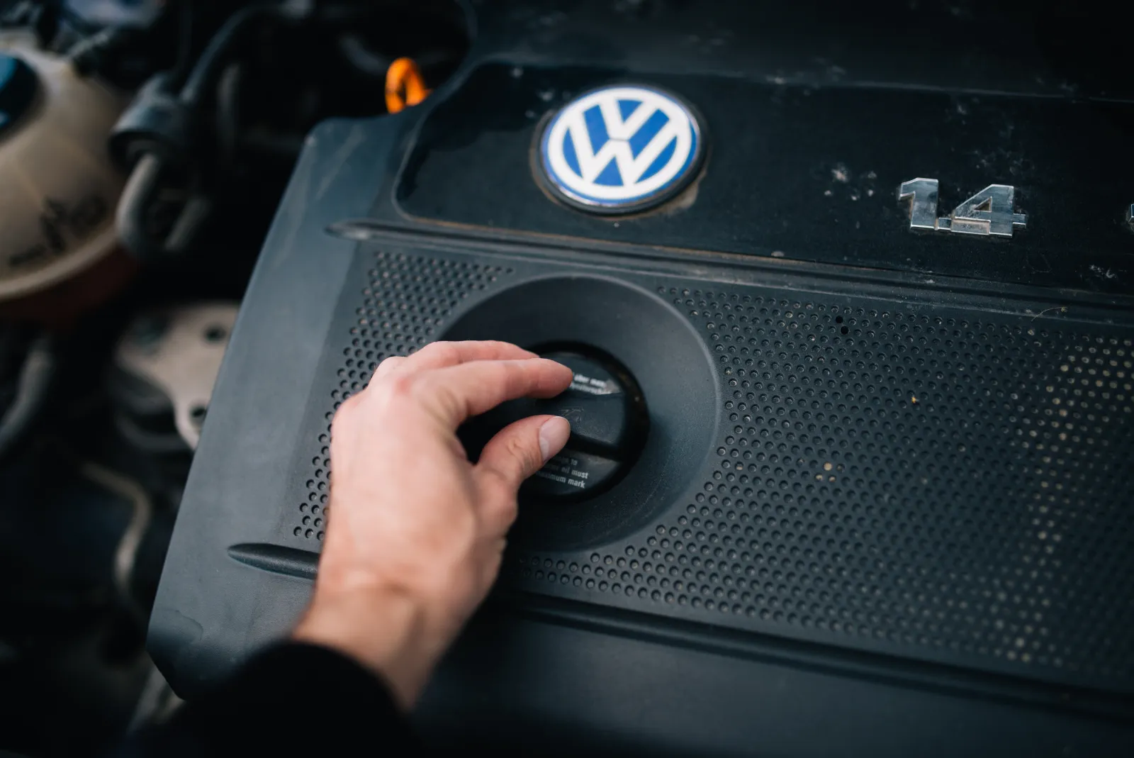 Mão abrindo a tampa do bocal de óleo sobre a capa do motor de um Volkswagen 1.4