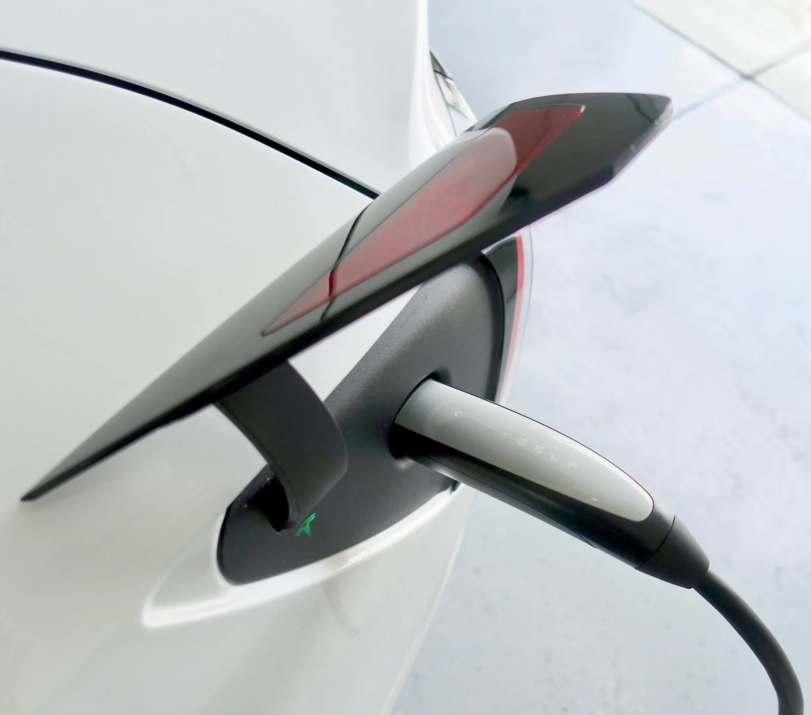 NACS connector seated in the rear charge port of a white Tesla Model 3