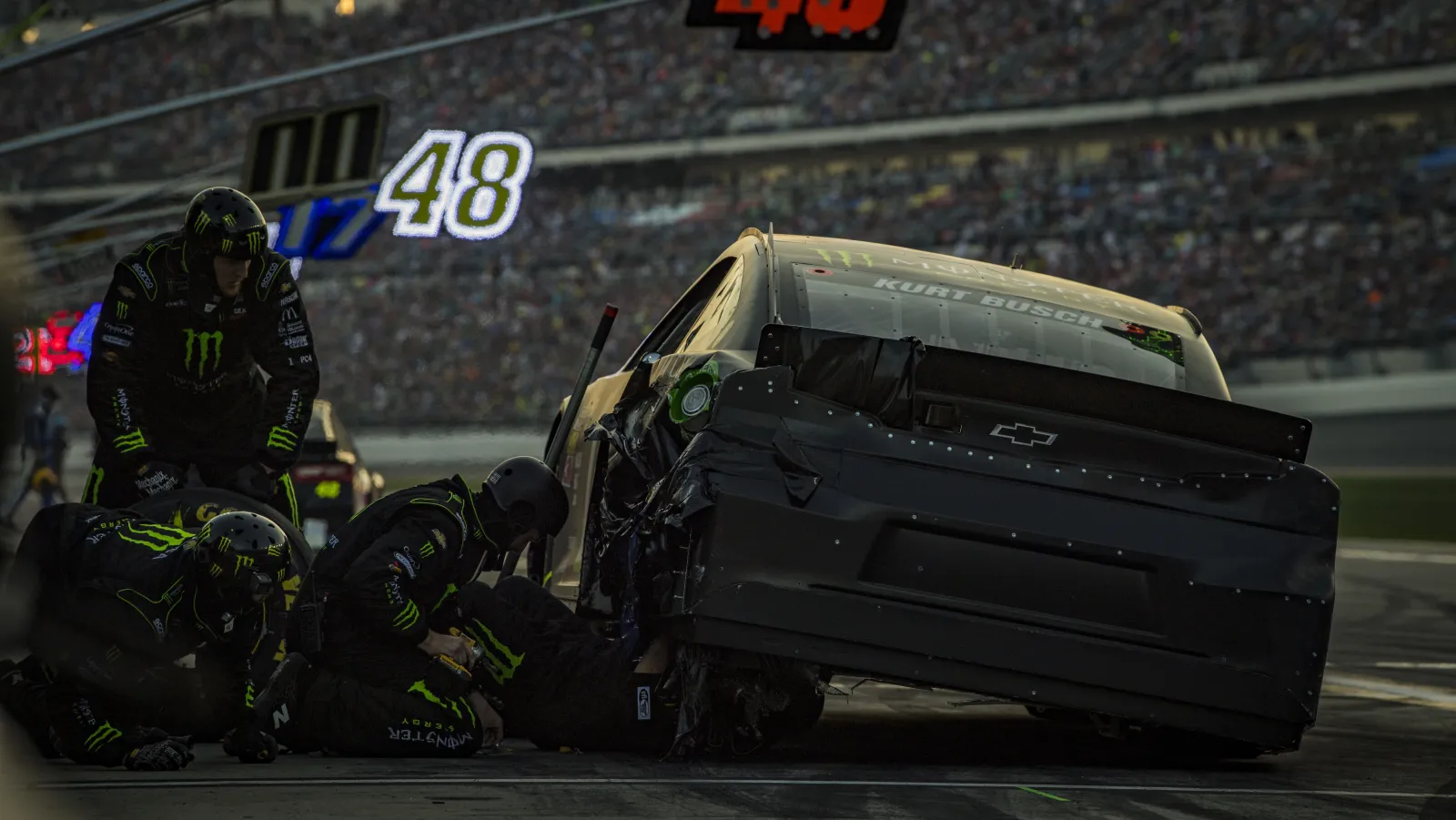 Cup pit crew repairing crash damage on a stock car on pit road at night