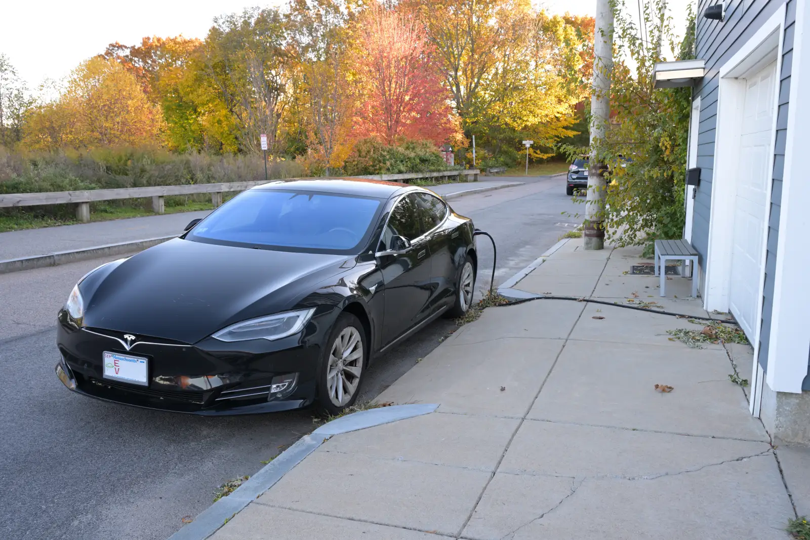 Black Tesla Model S plugged in beside a garage door on a residential driveway