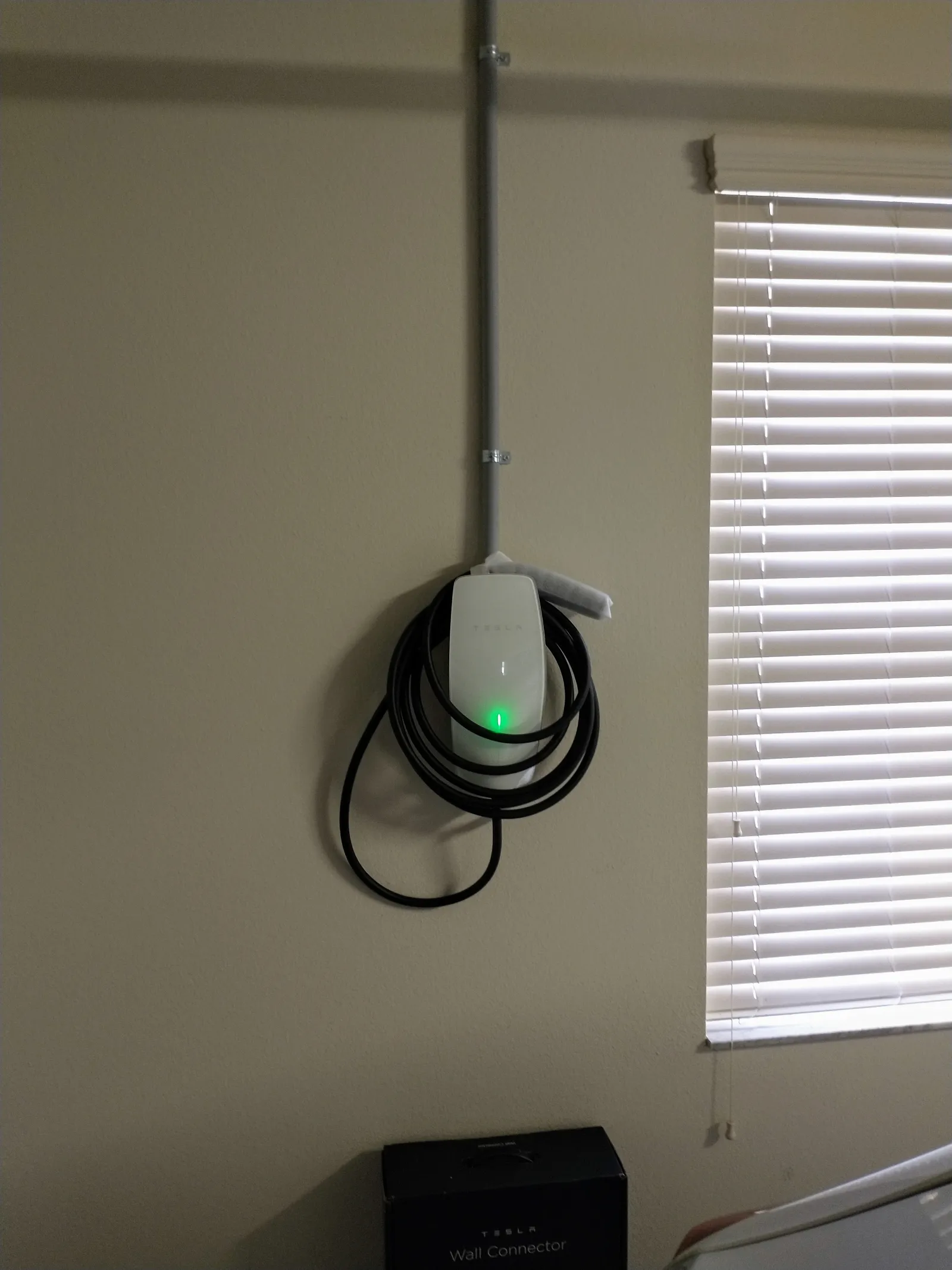 Tesla Wall Connector mounted on a garage wall with conduit and a coiled cable