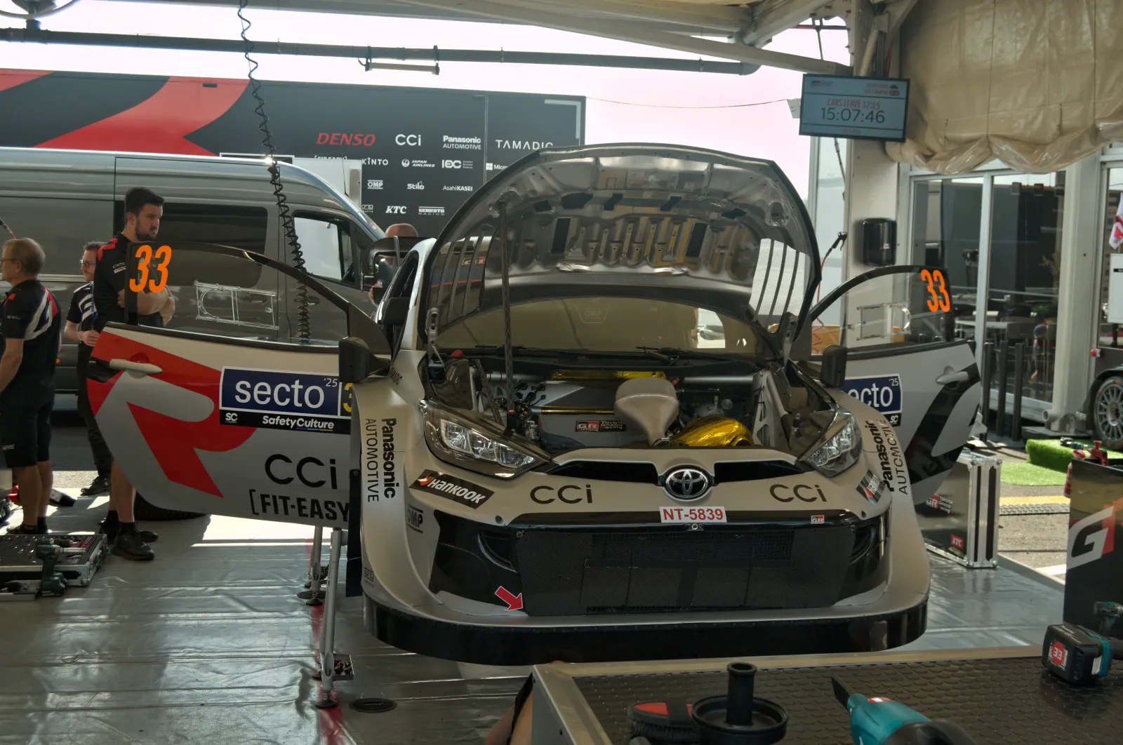 Toyota GR Yaris Rally1 with its bonnet open in the WRC service park, mechanics working around it