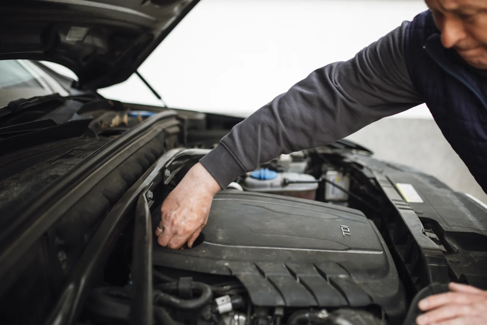 Technician leaning over an open bonnet checking engine components in a garage